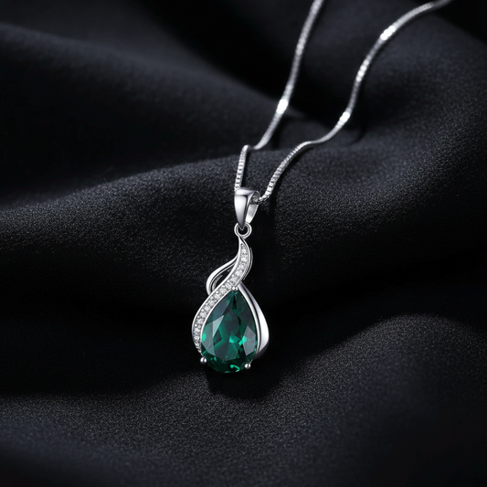 Silver necklace with a green teardrop pendant on a dark fabric background
