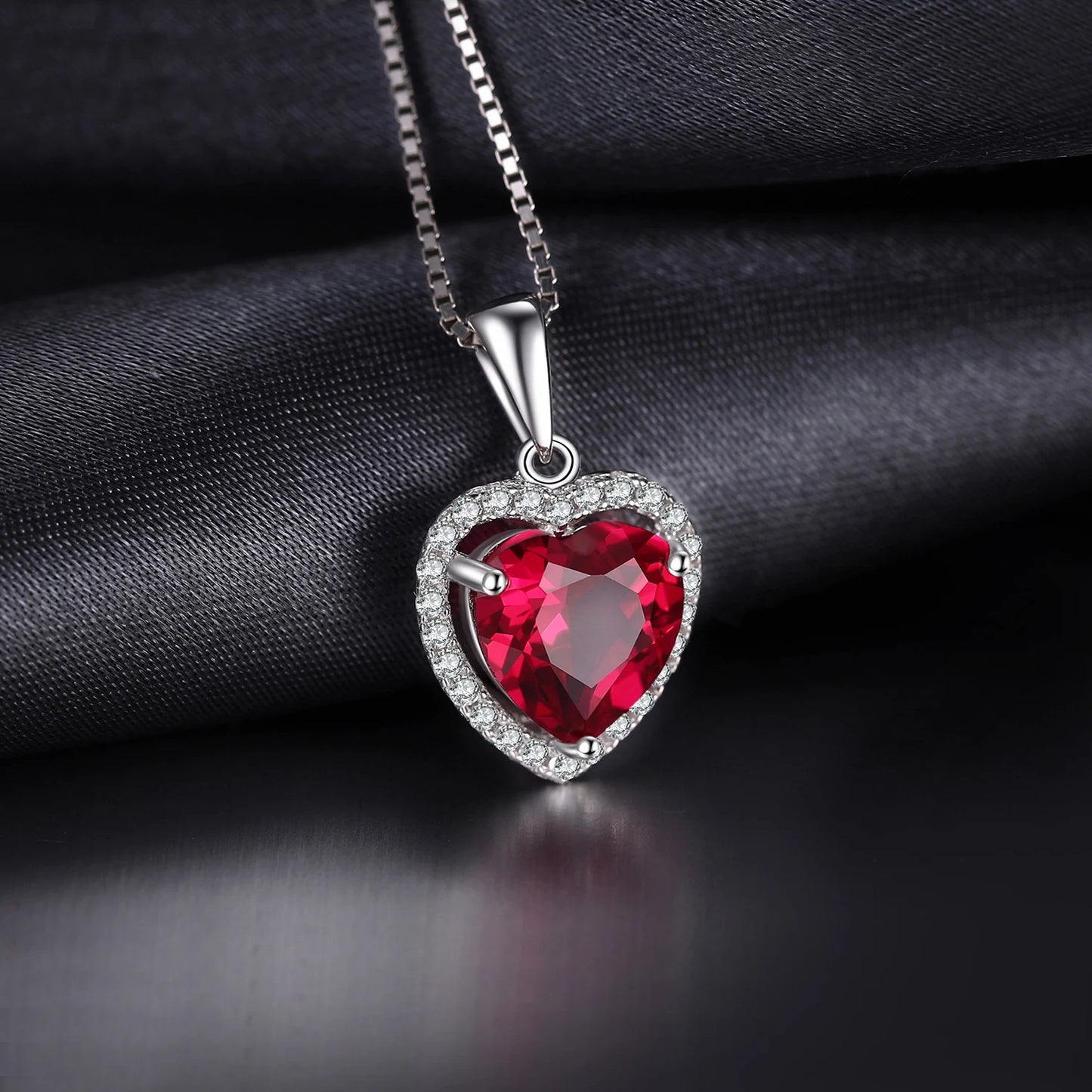 Elegant sterling silver heart pendant with a vibrant red lab-grown ruby and halo of cubic zirconia stones.