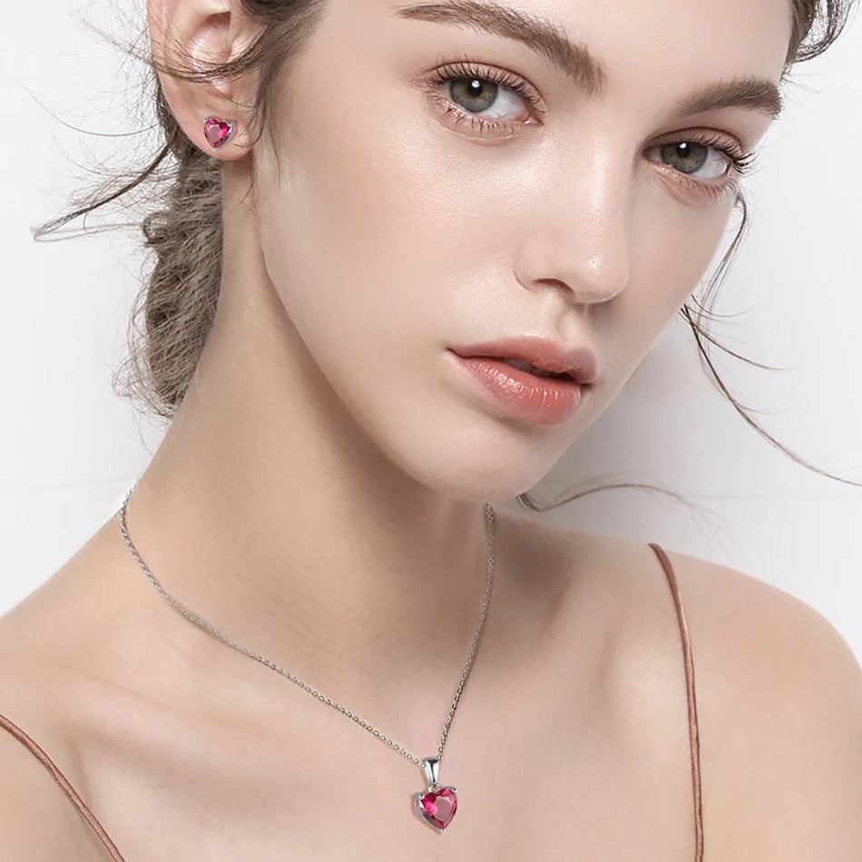 A woman wearing the Ruby Blossom heart necklace, showcasing its deep pink cubic zirconia stone in a sterling silver setting.