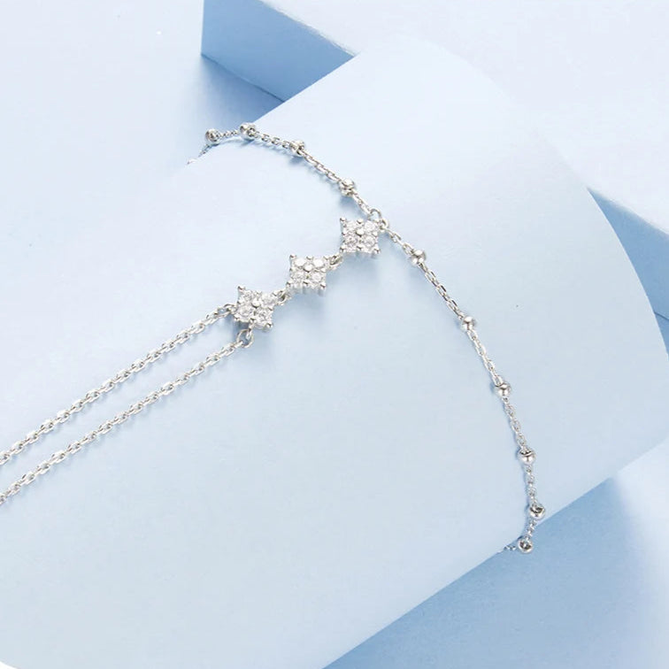 Silver bracelet with star-shaped charms on a light blue geometric background