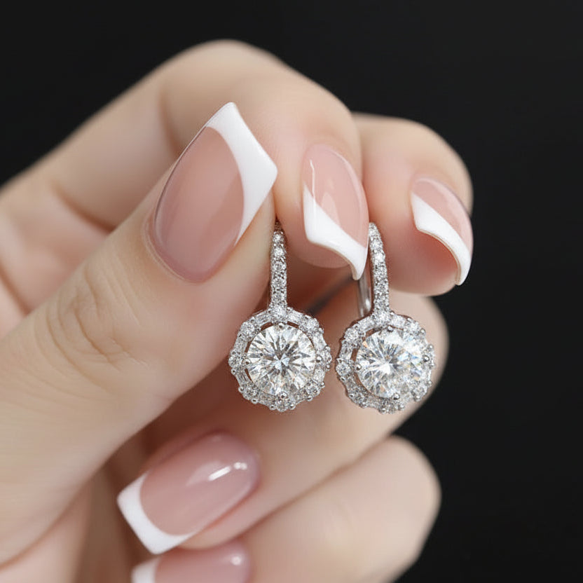 Versailles Halo Moissanite Earrings held by a hand in 925 sterling silver featuring a brilliant round center stone and mixed-cut halo