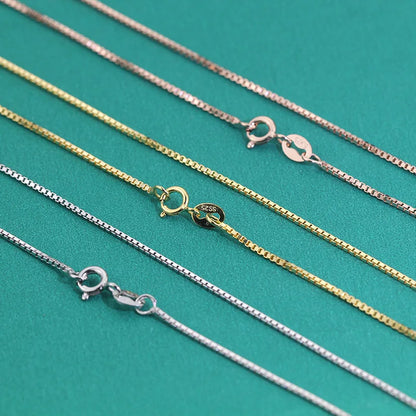Close-up of silver, gold, and rose gold box chains showing spring ring clasps side by side.