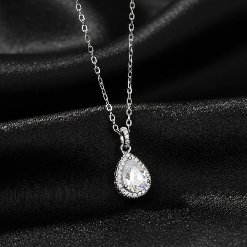Signature Moissanite pear halo pendant displayed on draped black silk to highlight the rhodium finish