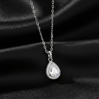 Signature Moissanite pear halo pendant displayed on draped black silk to highlight the rhodium finish
