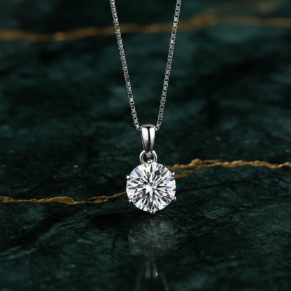 The Celeste Solitaire Moissanite Necklace by Ava Modus, displayed on a green marble surface to highlight the D-VVS1 stone's signature brilliance