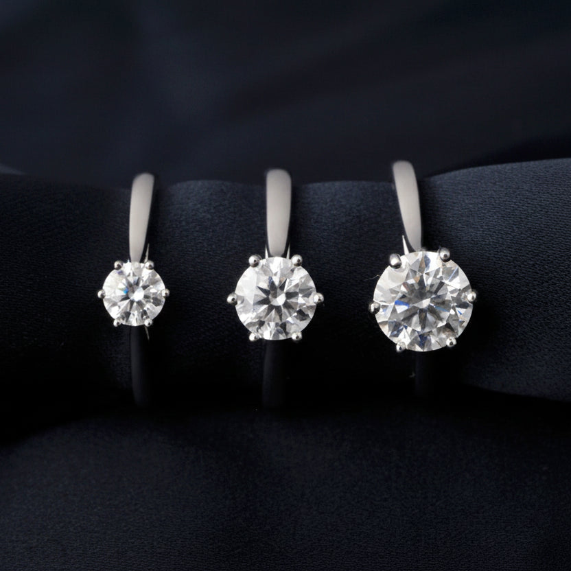 Three different sizes of moissanite rings on a black background