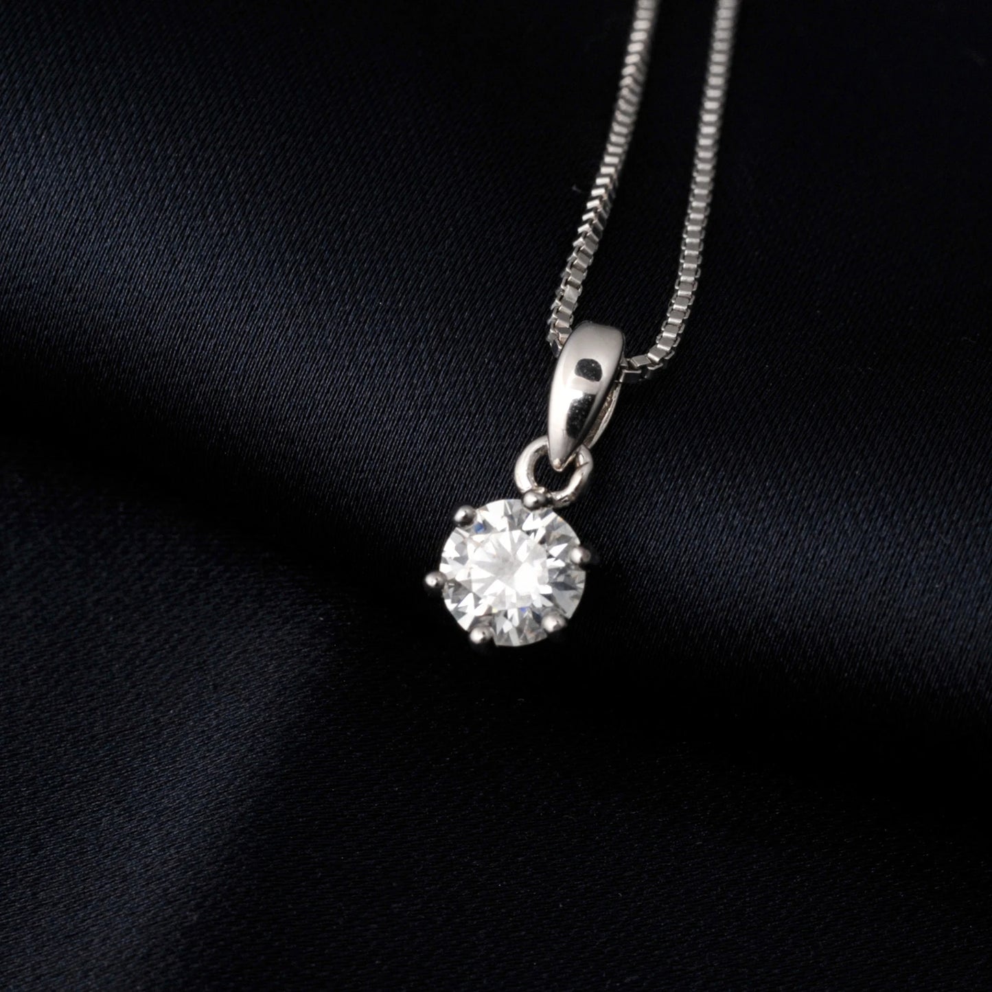 Silver necklace with a round moissanite pendant on a black fabric background