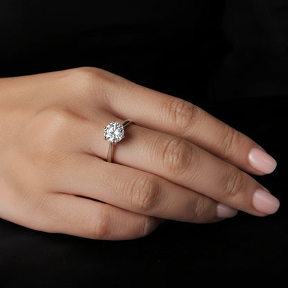 Hand wearing a silver moissanite ring on a black background