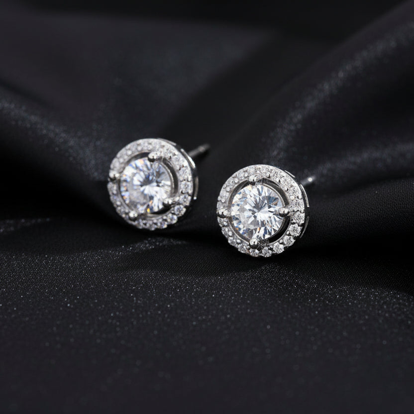 Artistic shot of the Pure Halo Studs nestled in black silk folds, highlighting the brilliant round-cut center stone